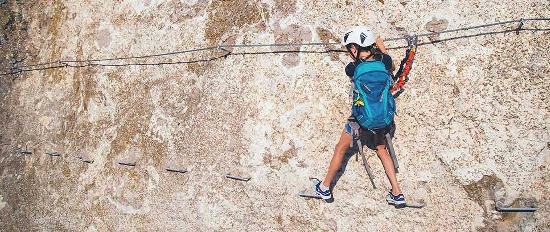 Una bambina dotata di attrezzatura percorre una ferrata in un geoparco